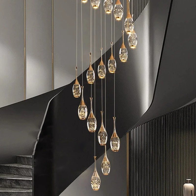 A cascading chandelier hung above a two-story entryway staircase, its multiple lit heads visible against a pale stairwell wall.